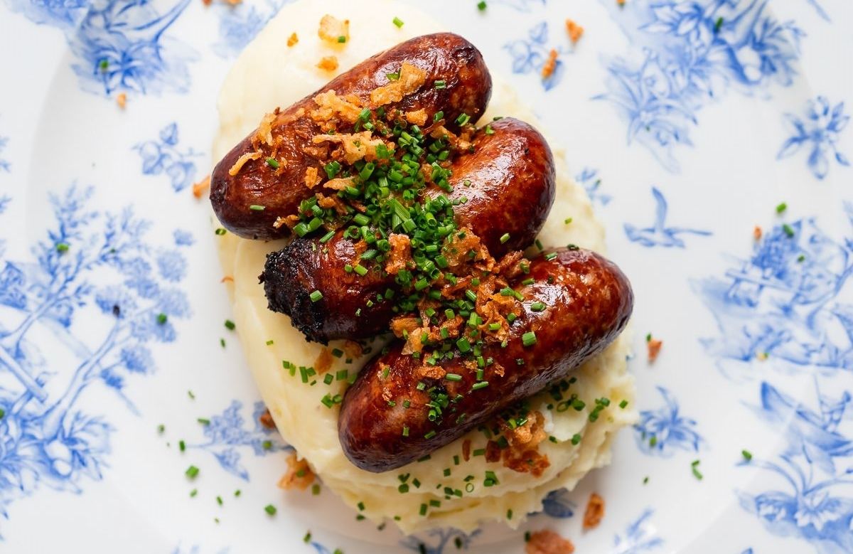 close up photo of sausage and mash potatoes on the white and blue plate