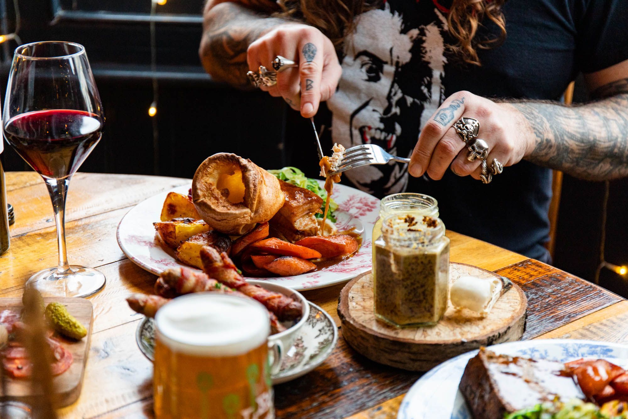 man with tattooed hands and rings on fingers enjoying his Sunday roast served with glass of beer at The Farm Tavern