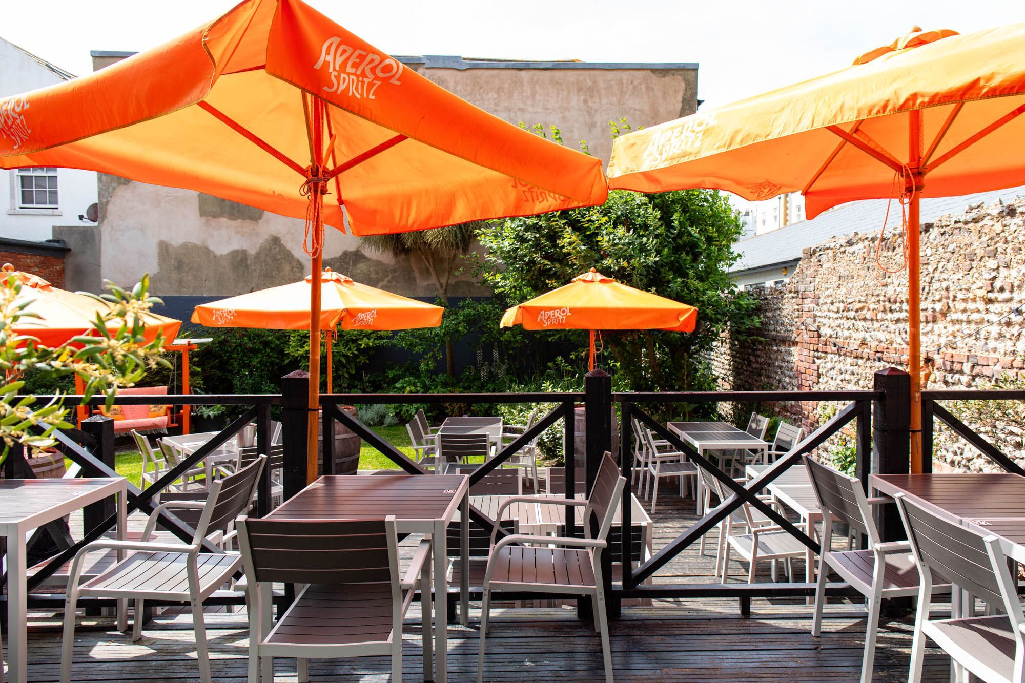 shot of the garden, brown chairs and tables with orange sun umbrellas
