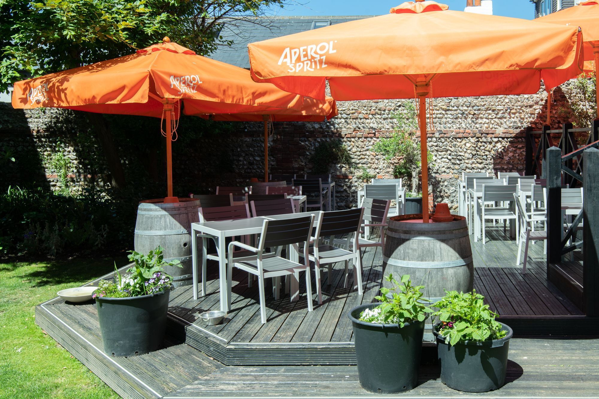 garden are of the daddylonglegs pub, grey and white chairs. orange parasols, green flowerpot