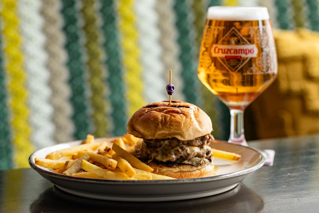 A plate of fries and a cheeseburger next to a glass of beer. Friends enjoying drinks and food at a Brighton pub with warm lighting and a relaxed atmosphere.