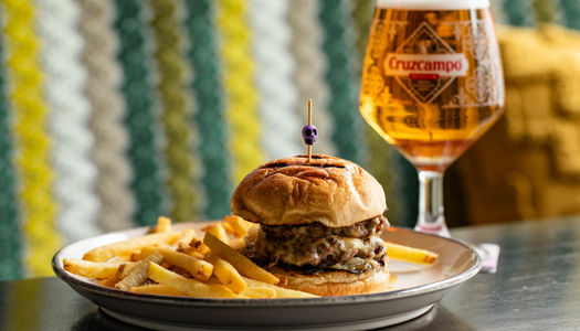 A plate of fries and a cheeseburger next to a glass of beer. Friends enjoying drinks and food at a Brighton pub with warm lighting and a relaxed atmosphere.