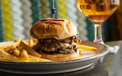 A close up shot of a burger inside a toasted bun with cheese and fries on the side.