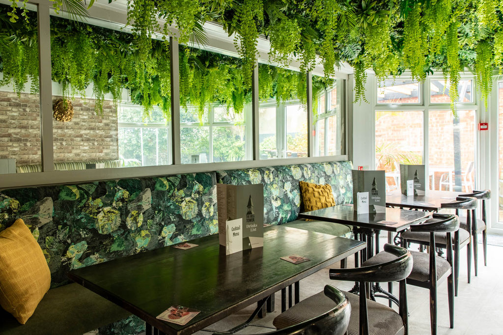 Inside The Bell Tower pub with foliage and green patterned wallpaper and dark wood tables and chairs.