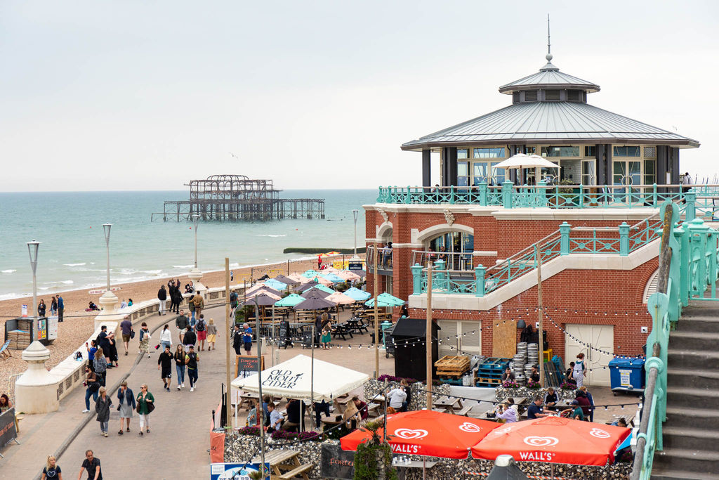 A view looking out over the derelict Brighton West Pier with a red brick rotunda in the foreground and stairs with light blue-green railings leading down from the main road to the seaside promenade