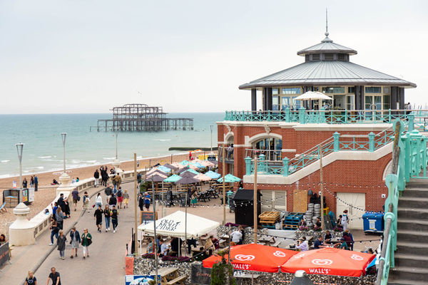 A view looking out over the derelict Brighton West Pier with a red brick rotunda in the foreground and stairs with light blue-green railings leading down from the main road to the seaside promenade