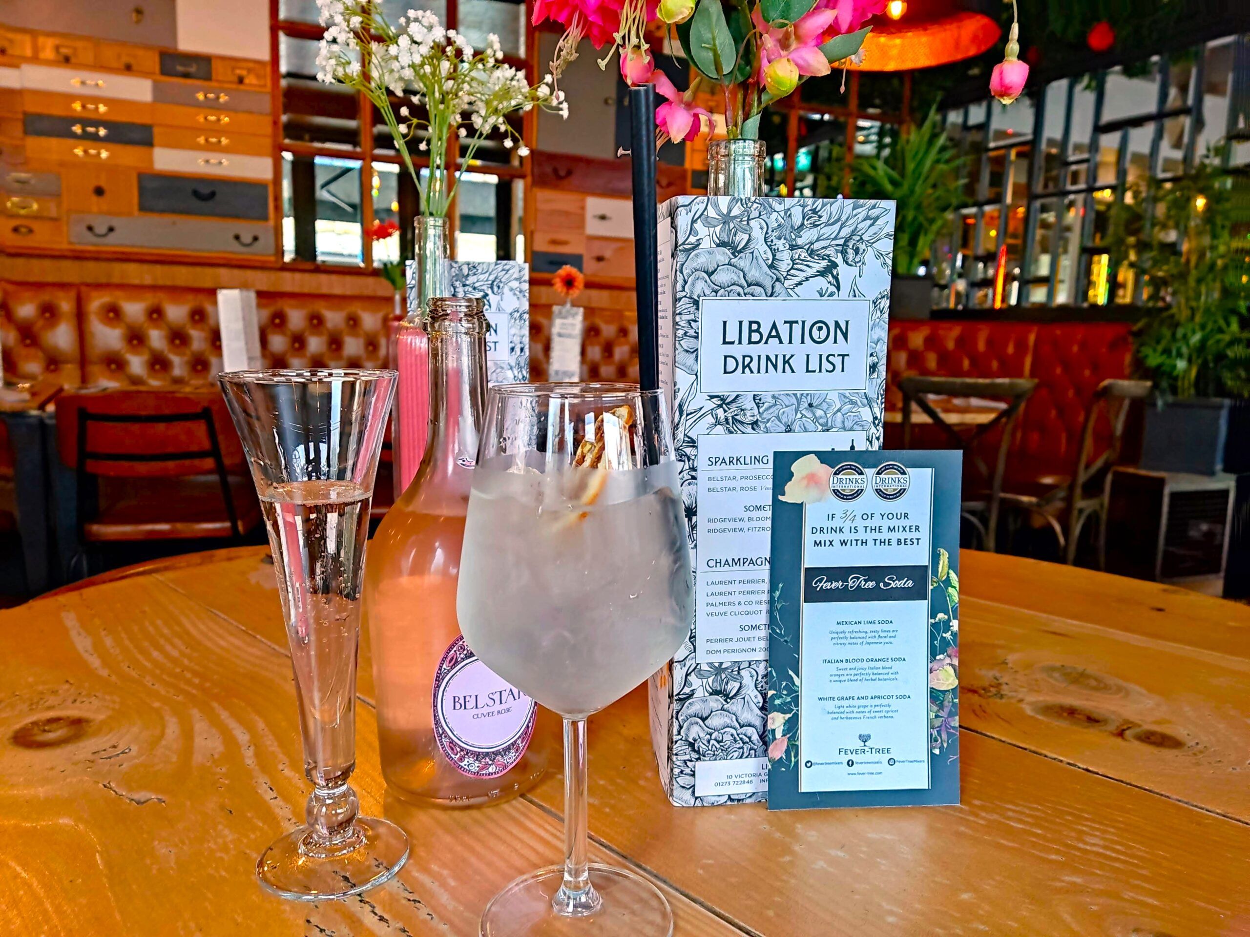 libation drink menu on the brown table together with the bottle of delicately pink Belstar, and two glasses 