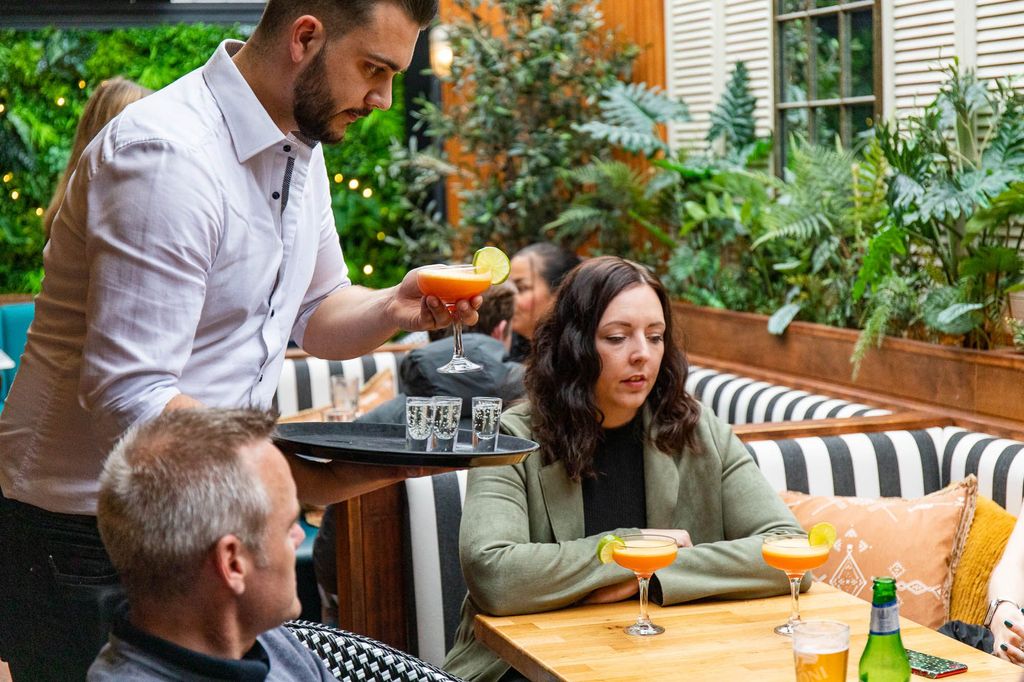 Bartneder serving two people with their red cocktails and shots