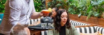 Bartneder serving two people with their red cocktails and shots