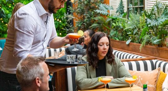 Bartneder serving two people with their red cocktails and shots