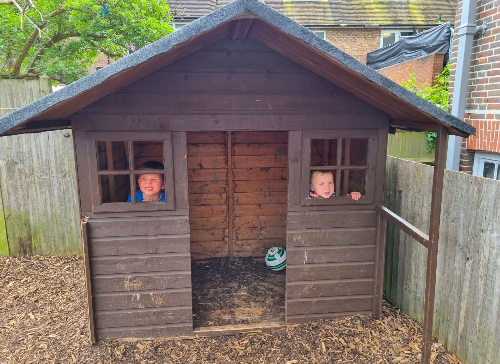 two kids looking through the window of the small wooden playhouse