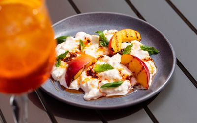 white dish with nectarine pieces on the top served with aperol spritz at DaddyLonglegs