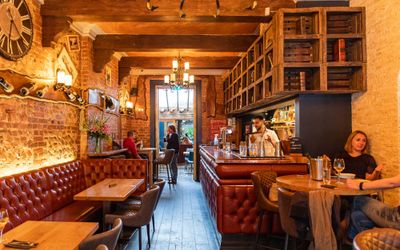 interior of the paris wine bar,wooden ceiling and bar shelves, brown table with chairs arround and red dinners attached on the wall, romantic restaurants Brighton