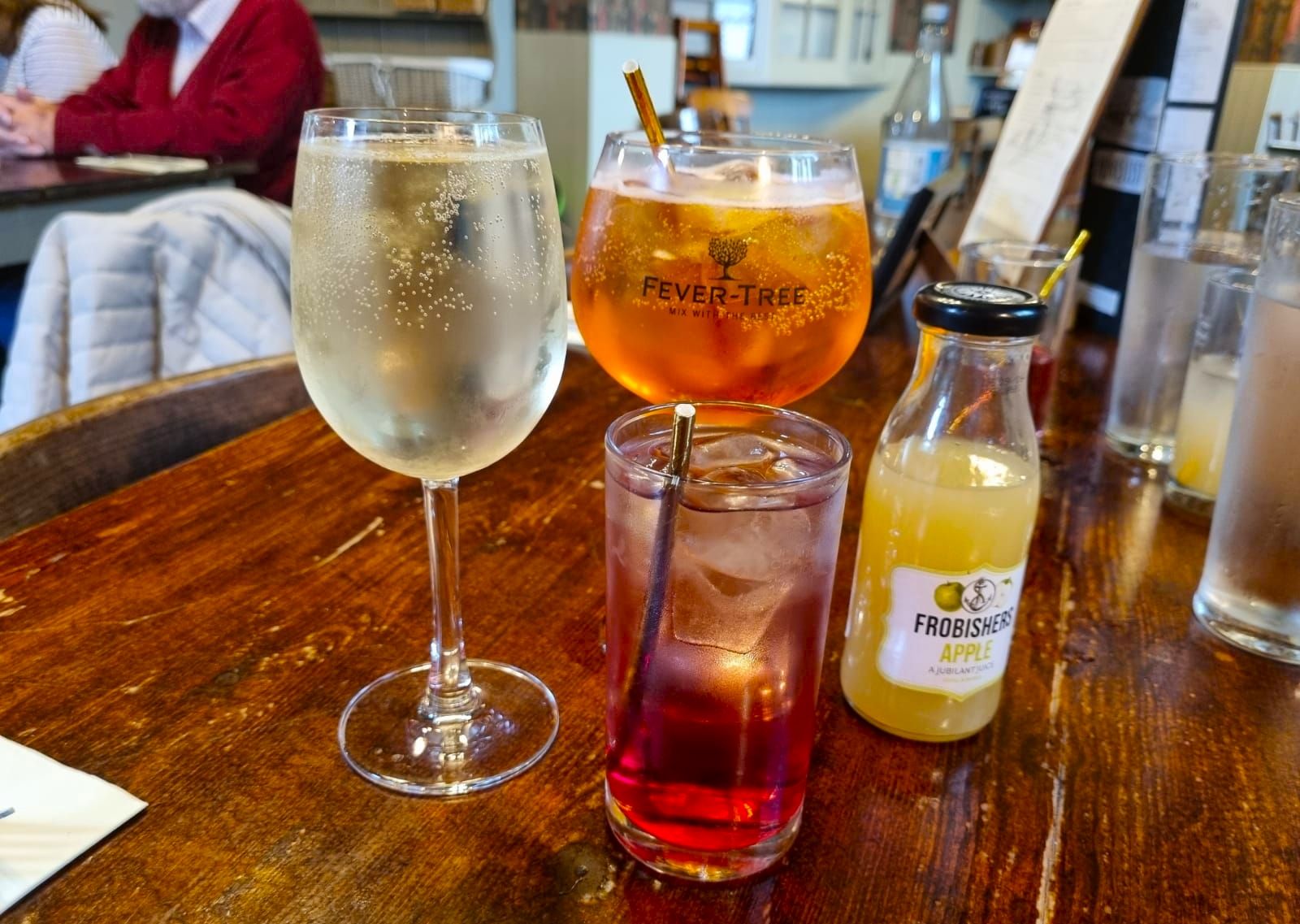 five different drinks on the brown table, including apple juice, apperol sprizt and wine