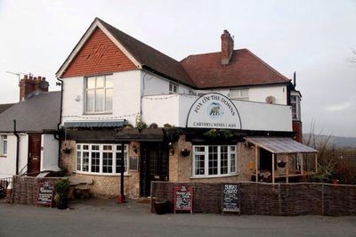 The Fox on the Downs pub from the outside, the lower half is yellow brick with pay windows and a side seating area, the second floor is white washed with a balcony and a red tile roof