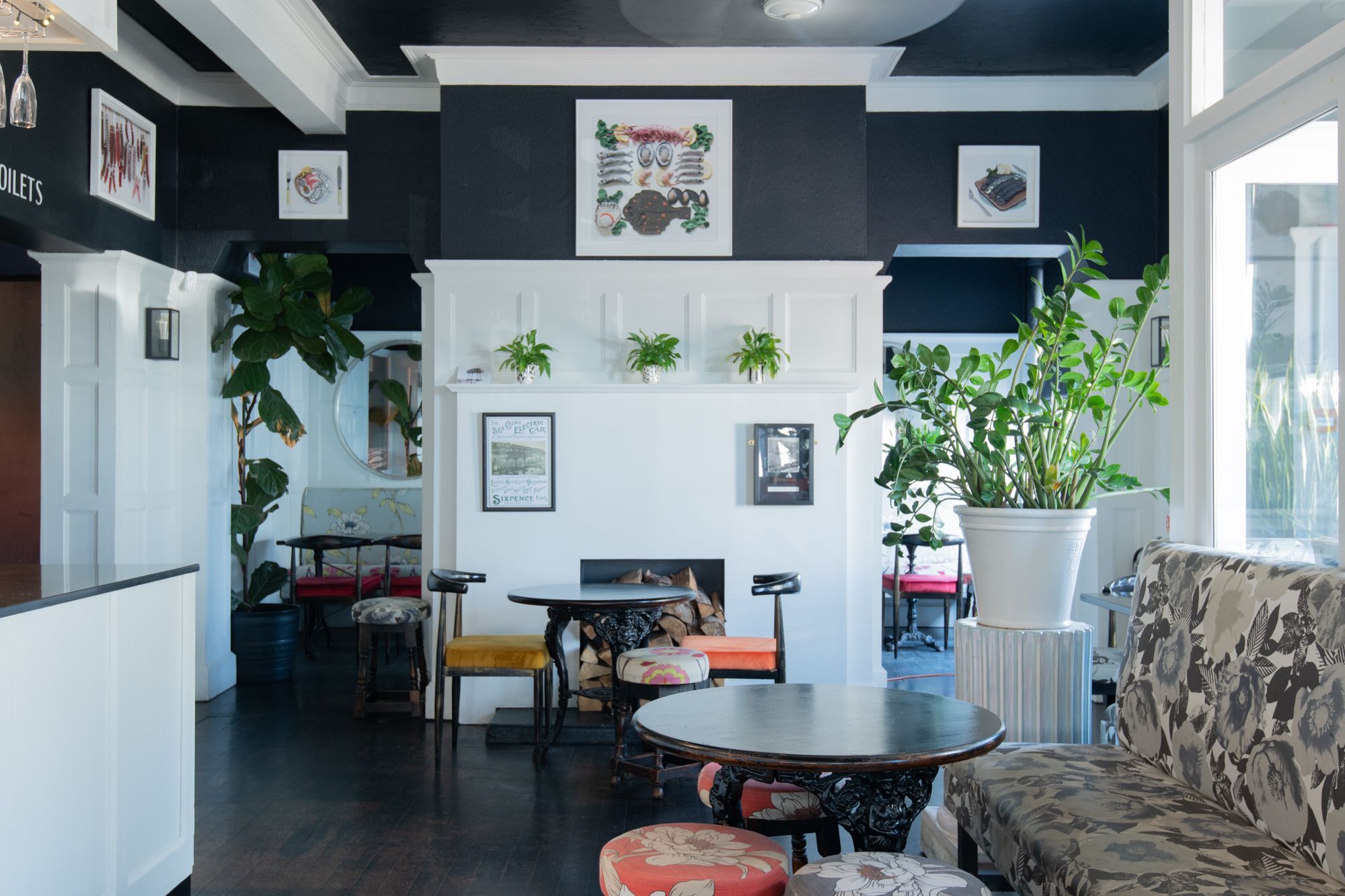 black and white walls of the daddylonglegs pub, plants decoration on the wall, dark brown tables, orange and pink chairs, flower decorated diners