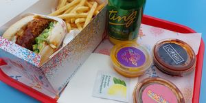A burger and chips in a takeaway box, with a can of Ting and three sauces