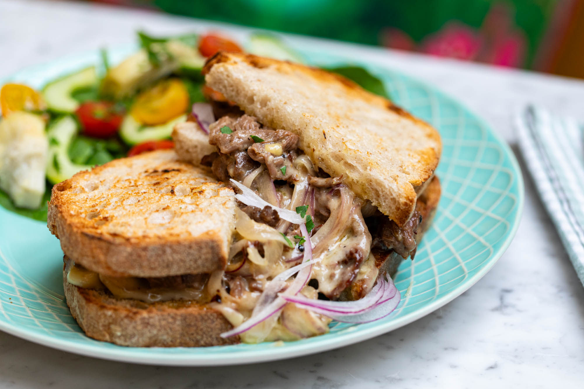 A vibrant photography of a sandwich cut in half on a blue plate with a side salad.