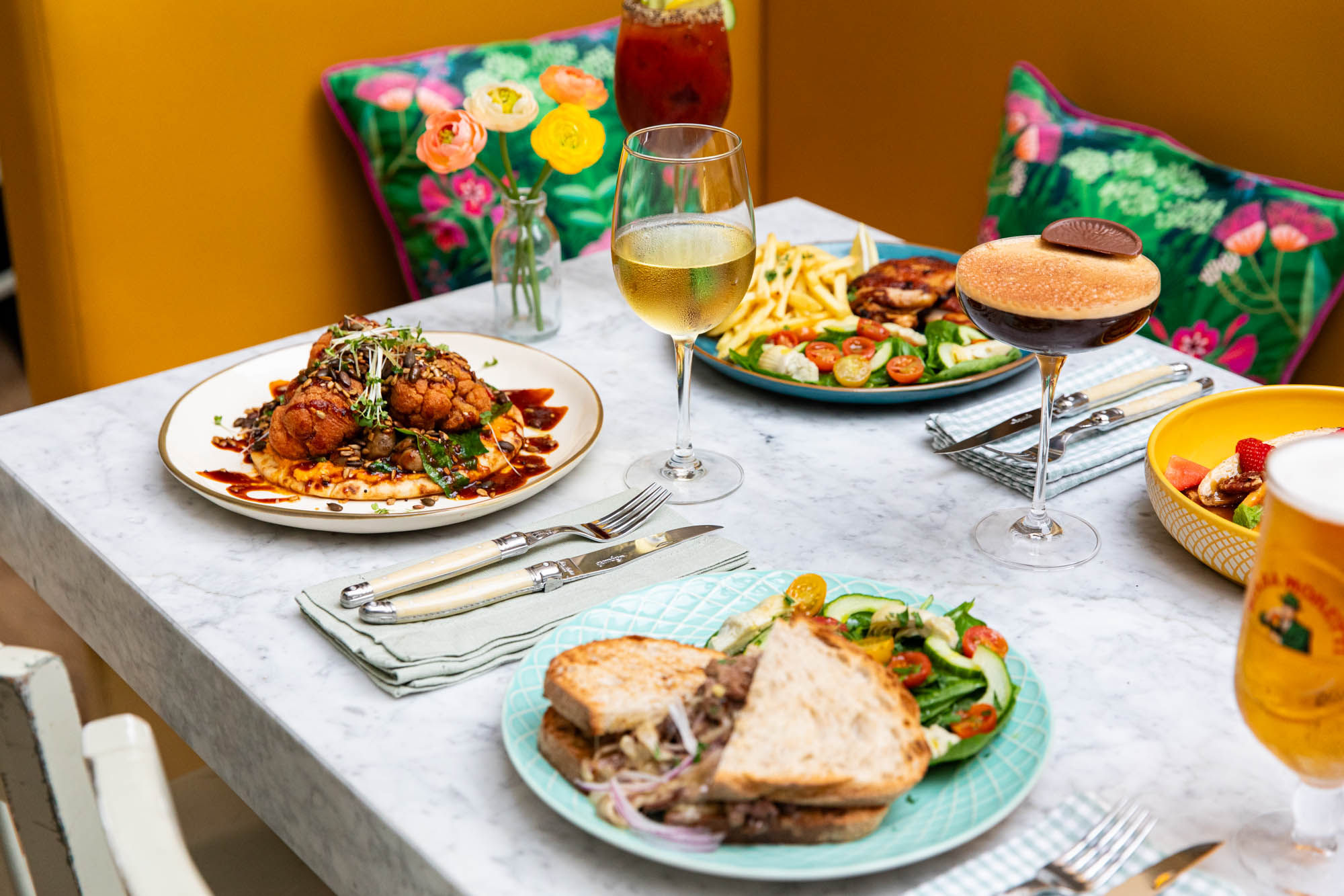 Plates of colourful food served on a marble table with a vibrant cushion in the background.