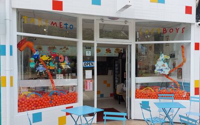 A white fronted chicken shop with blue tables and charis out the front. The window display is full of orange balls and there are cartoon characters on the windows