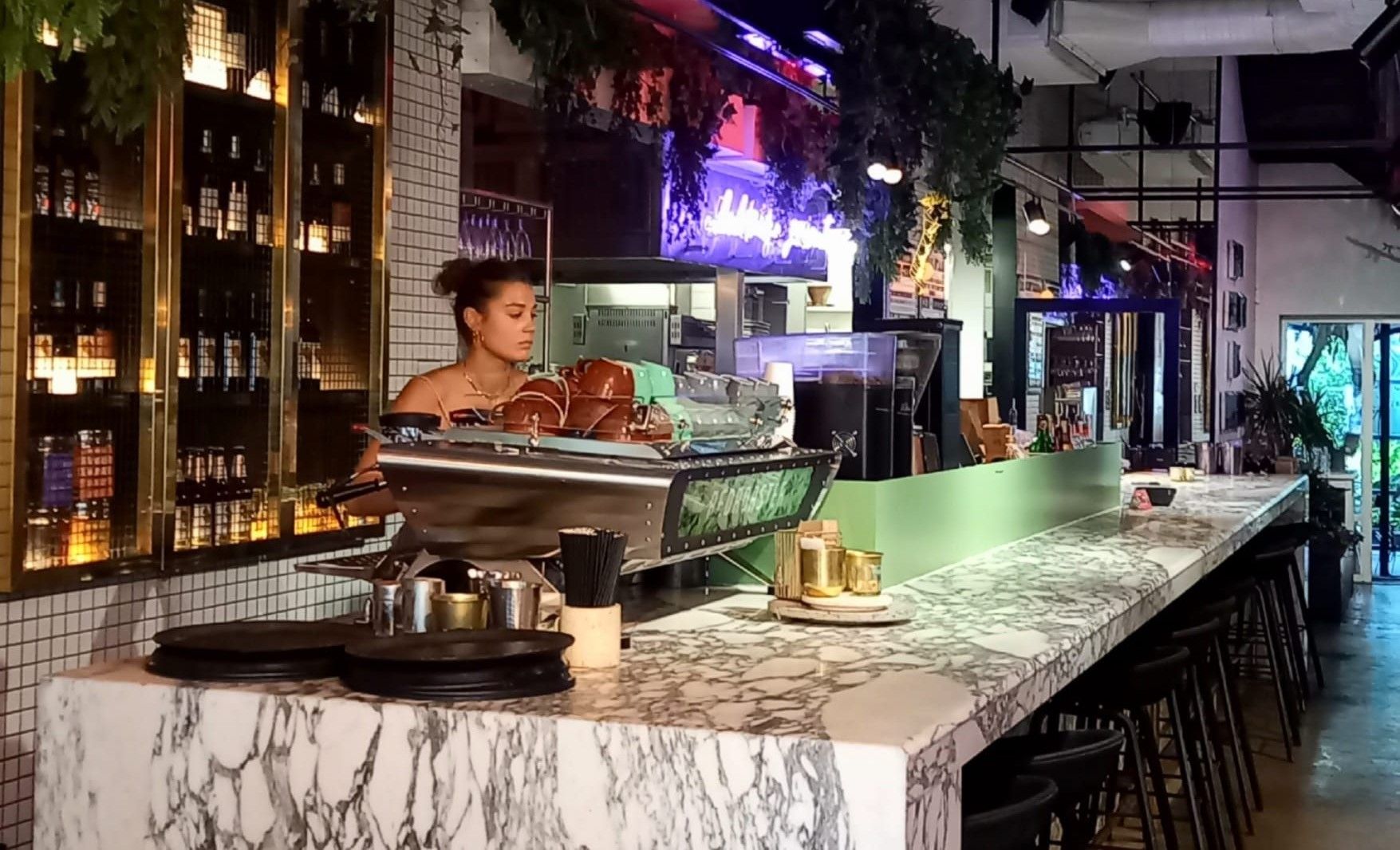 bar area at Lucky Khao. a Northern Thai restaurant offering a Brighton BBQ style food offering. The bar area is a classic looking marble top with plant foliage and neon lights. 