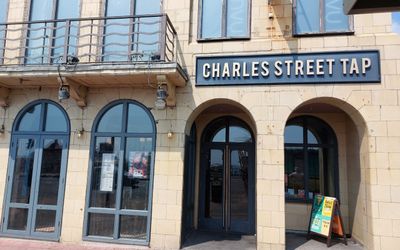 The ouside or a yellow brick building with arched windows and a doorway and a sign reading Charles Street Tap. Gay Bars Brighton Guide. LGBTQ+