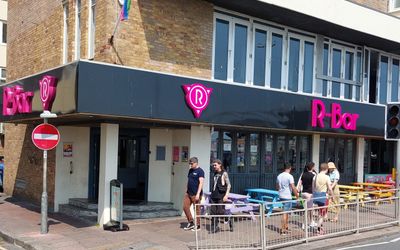 People walknig past rainbow coloured benches outside R-Bar on Brighton seafront