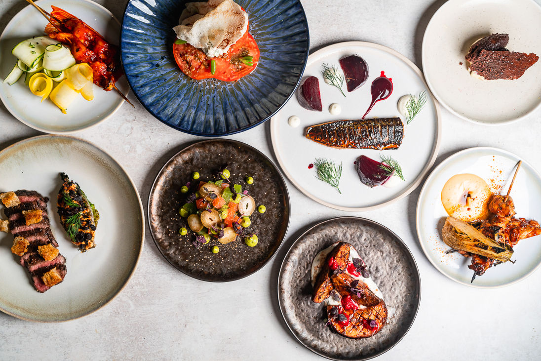 Overhead shot of eight assorted plates, including fish and steak and grilled vegetables