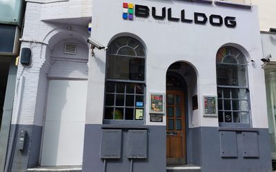 The exterior of a bar with the lower half in dark grey and the upper in lilac-grey and arched windows and a sign reading Bulldog