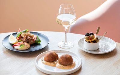 three small white plates with different food and hand holding glass of white wine