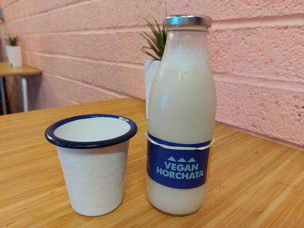 A glass bottle containing vegan Horchata and a white and blue enamel cup