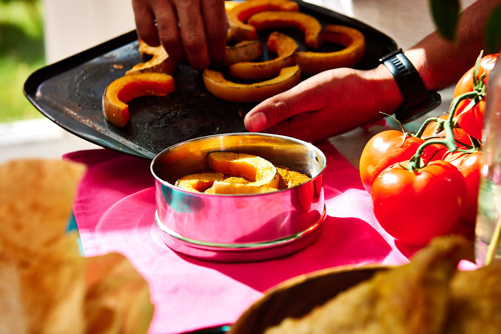 Slices of roasted squash being placed onto a curry in a tiffin container.