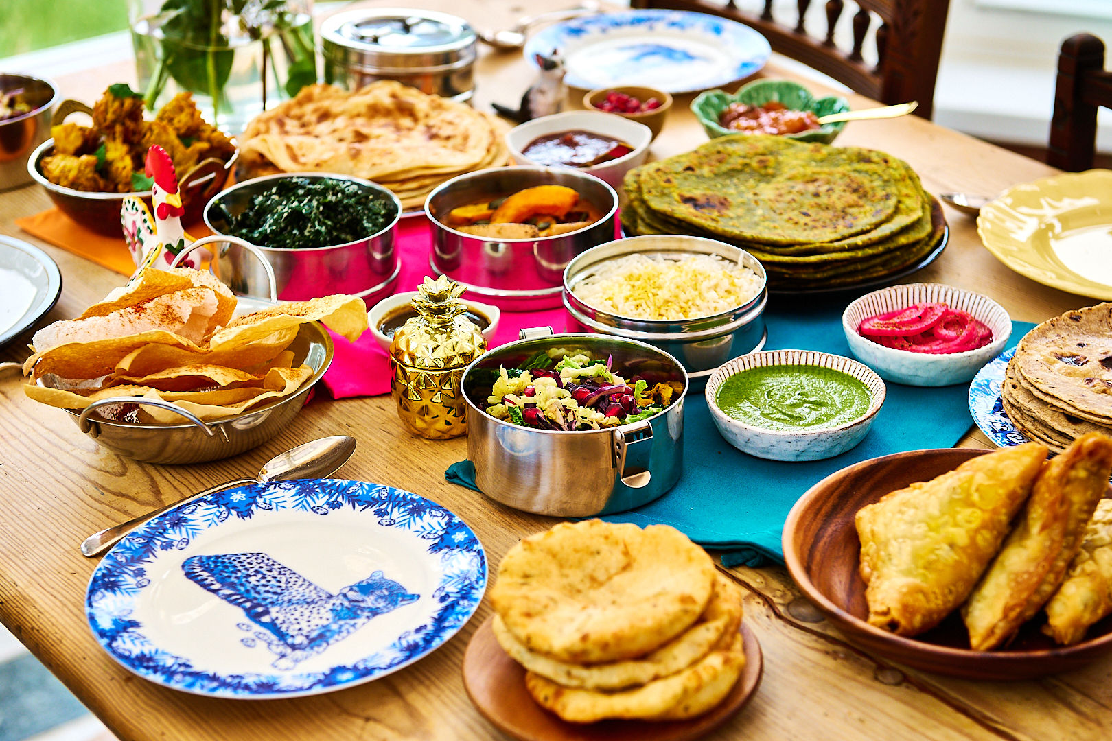 Lots of dishes laid out on a wooden table to plates and sides dishes and breads.
