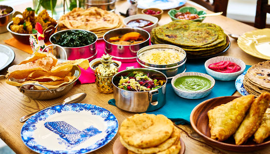 Lots of dishes laid out on a wooden table to plates and sides dishes and breads.