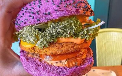 A purple burger bun filled with curly lettuice, a plant based patty and sauces