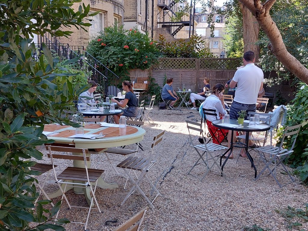 A pebbled walled garden with round metal tables set for eating. A few tables have groups at them already