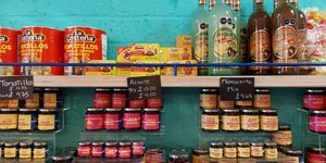 shelves lined with jars of salsa and giant tins of green tomatoes and white beans with hand written price labels on black card