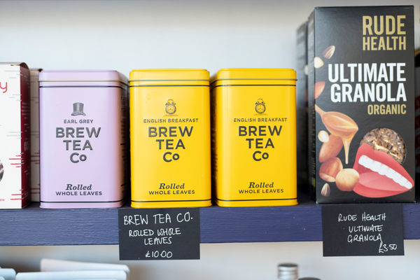 Square metal tins of Brew Tea Co tea and a box of granola on a shelf