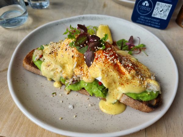 Toast topped with avocado, white crab meat and two poached eggs is smothered in thick lashings of creamy yellow hollandaise sauce and a sprinkling of deep red paprika. Queens Park cafe