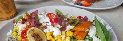 A colourful plate of avocado on toast with sweetcorn, sweet potato, feta and chillis, behind is another plate of American pancakes with berries and banana and another with an egg Benedict