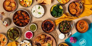 over head shot of a table laid out with Majahma tiffins filled with the food and sauces. There are glasses of water on the table too. Winner of Best Takeaway in Brighton. BRAVO 2025