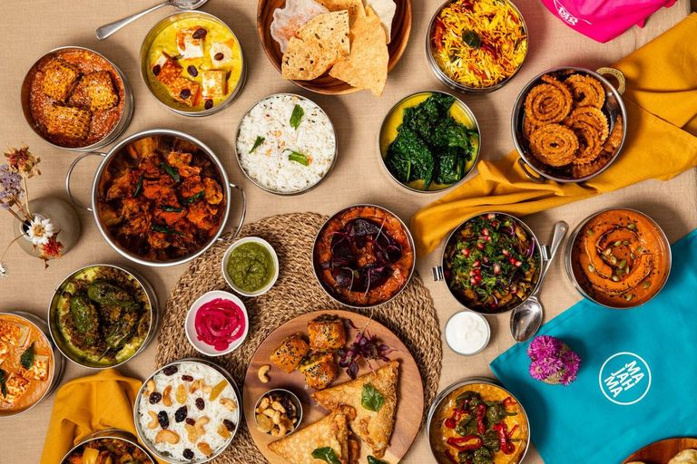 over head shot of a table laid out with Majahma tiffins filled with the food and sauces. There are glasses of water on the table too. Winner of Best Takeaway in Brighton. BRAVO 2025