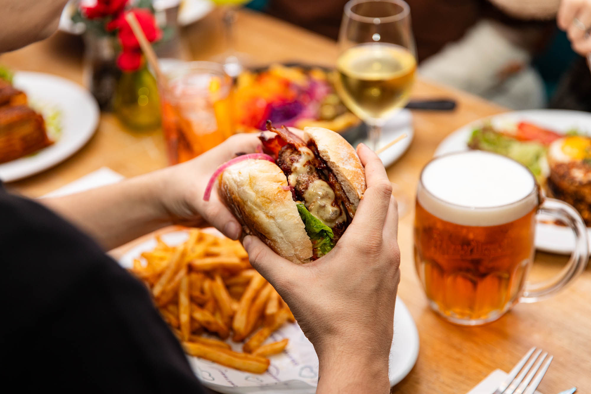 A person eating a burger with fries and a glass of beer at Arcobaleno in Brighton.