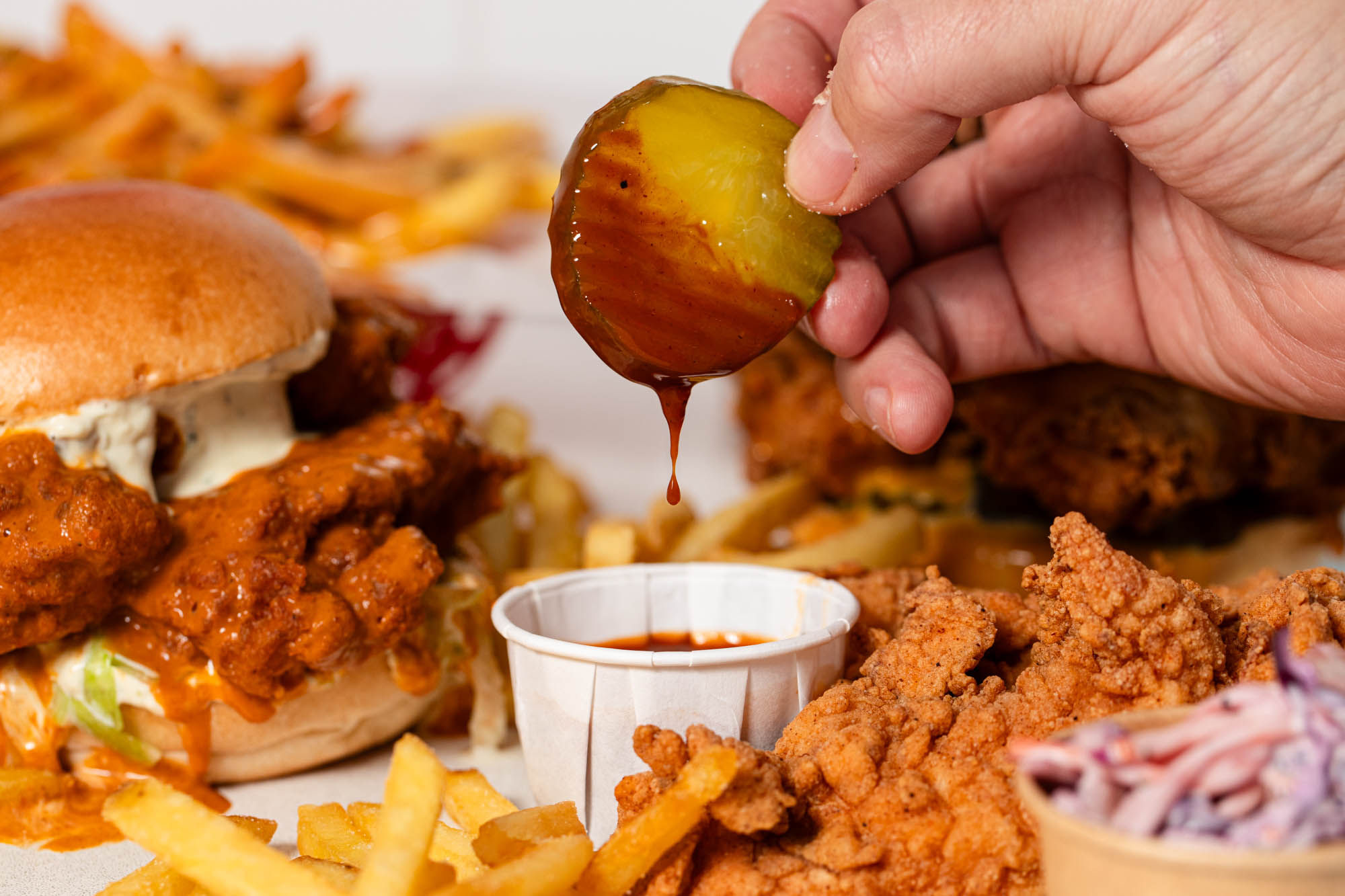 hand holding pickle being dipped in sauce at Lost Boys Land 