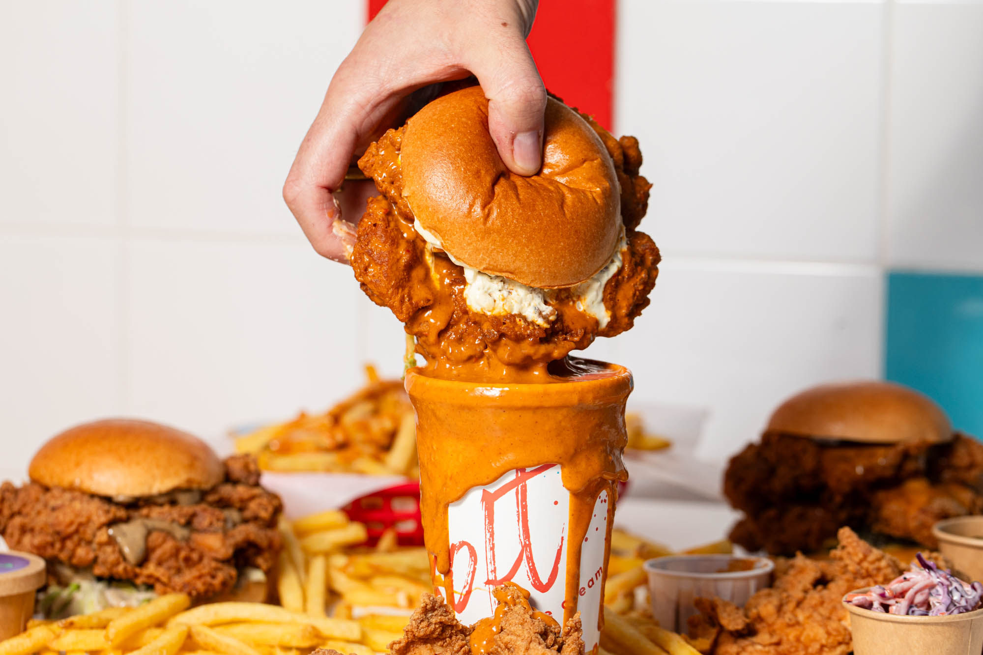 Lost Boys Land fried chicken burger being dipped in the cup full of sauce, lots of chips on the table