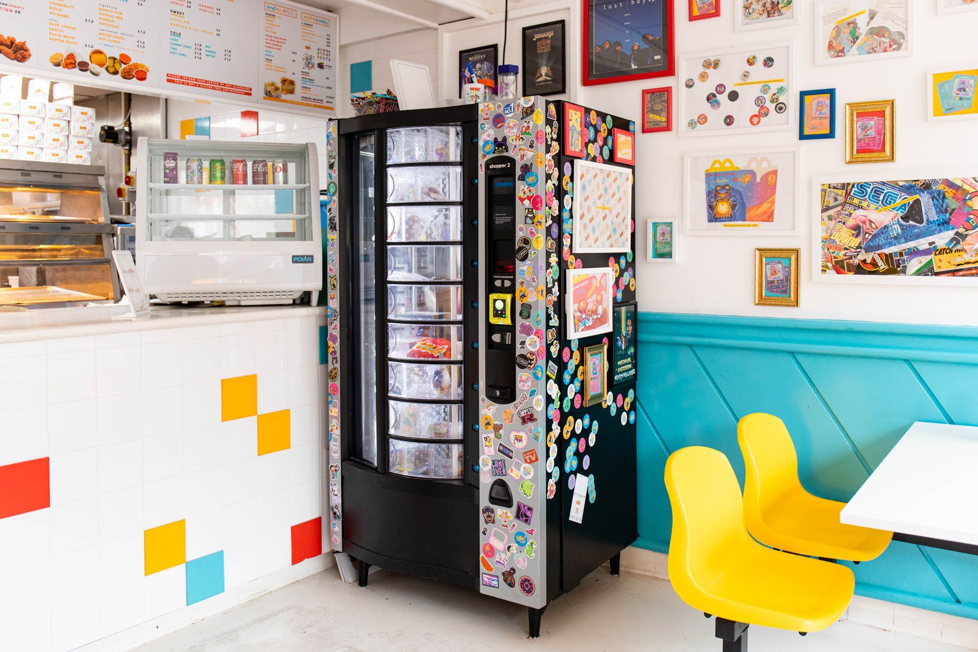 Lost Boys Land vending machine in the corner of the food shop, white tables and yellow chairs, walls decorated with various pictures