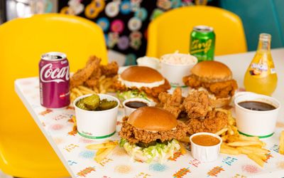 Lost Boys Land table filled with three different chicken burgers, chicken wings, sauces, and cherry Coca Cola, sprite and orangina. Listed in our places to eat in Brighton