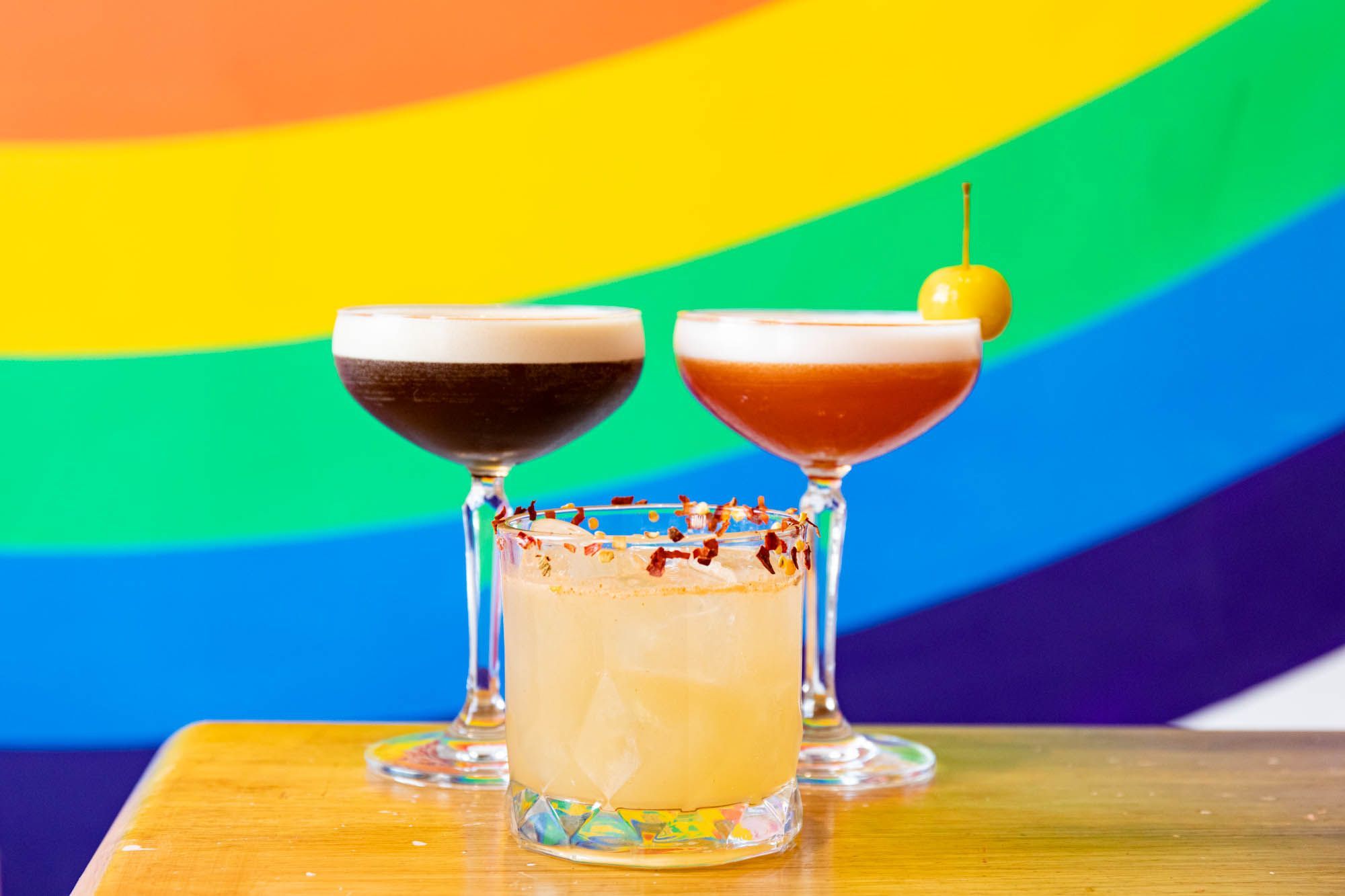 three cocktails on the wooden table with rainbow background