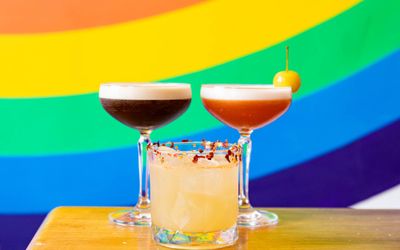 three cocktails on the wooden table with rainbow background.