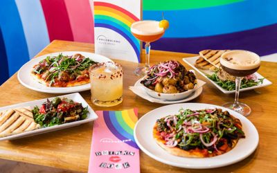 side shot of the colorful table filled with plates of food and glasses of cocktails, rainbow background